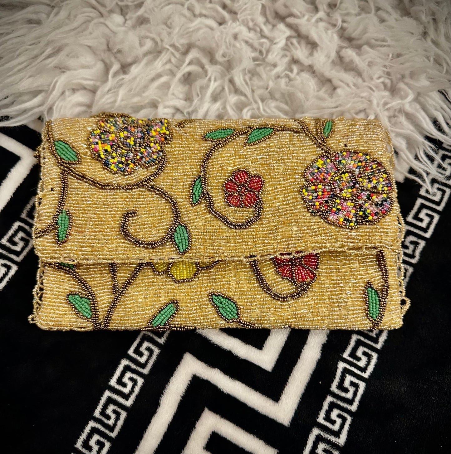 An exquisite gold beaded envelope clutch purse featuring colorful hand-embellished floral patterns and green leaf motifs. Crafted by Amal Ayub, this luxury accessory is a perfect addition to premium Ladies Hand Bags Pakistan
