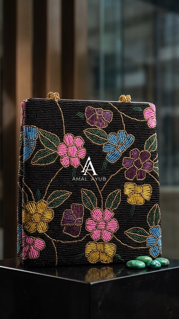 Amal Ayub black embellished handbag featuring handcrafted pink, blue, and purple floral beadwork with gold-braided handles