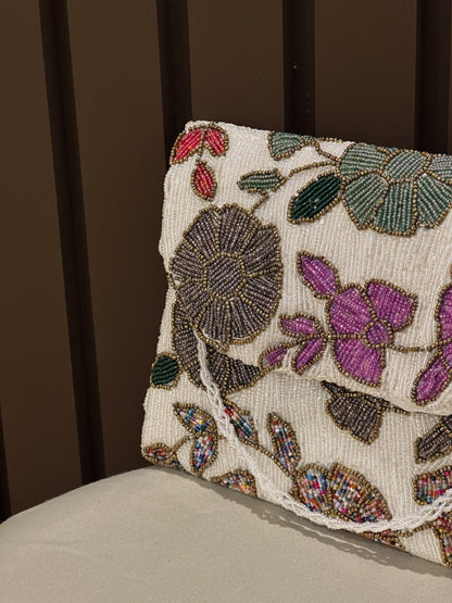Hand-beaded floral clutch bag with purple and pink embroidered flowers on a cream base by Amal Ayub