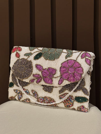 Hand-beaded floral clutch bag with purple and pink embroidered flowers on a cream base by Amal Ayub
