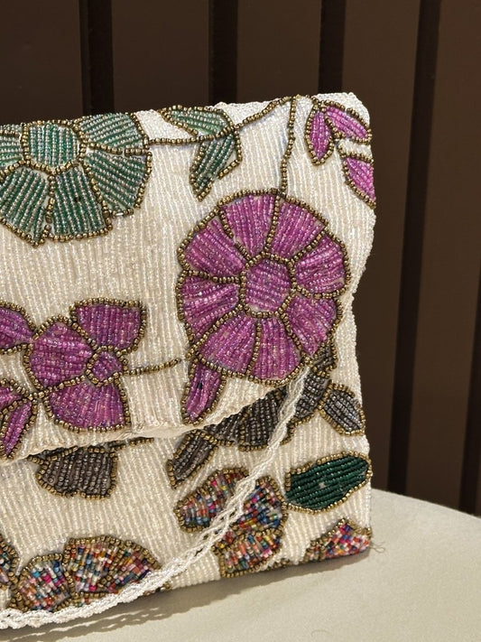 Hand-beaded floral clutch bag with purple and pink embroidered flowers on a cream base by Amal Ayub